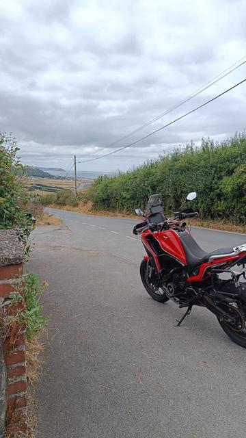 Red motorcycle on the side if a road leading down to a village by the sea